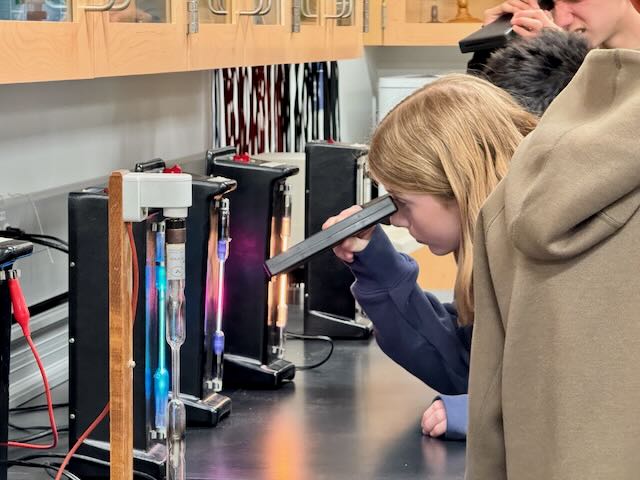Student staring through a prism to see atomic emission spectra.