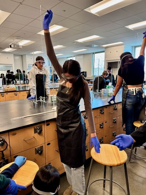 Student stretching out a string of synthesized nylon with arm extended high.